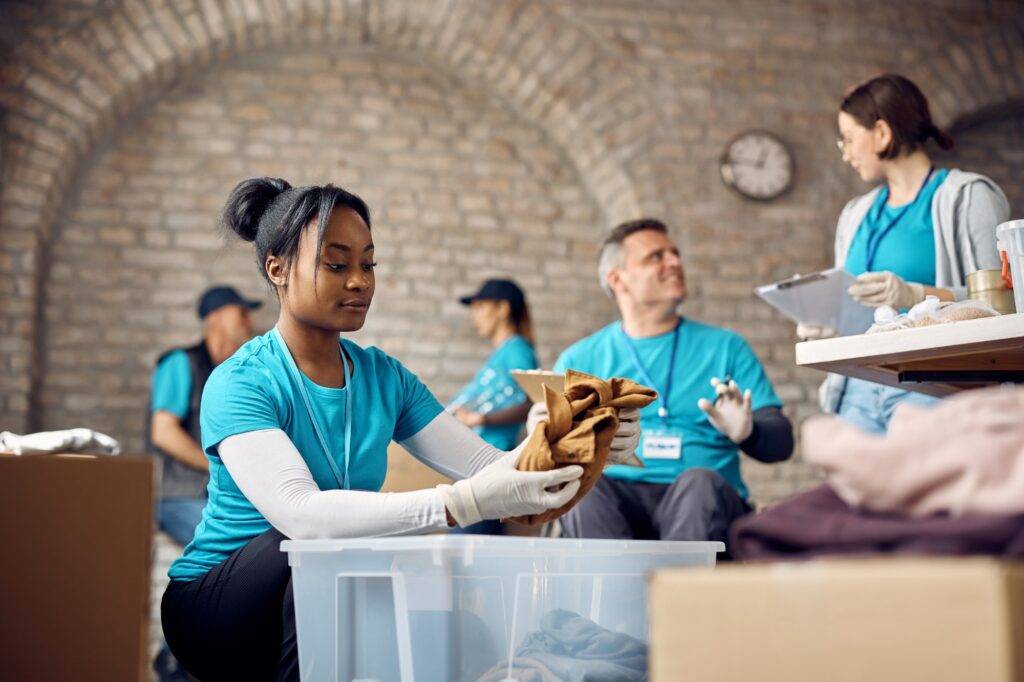 Young African American volunteer packing donated clothes into boxes.